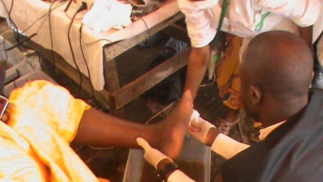 A volunteer's gloved hands caring for someone's foot at a community health day